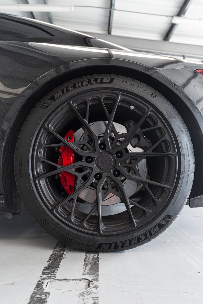 Detailed view of a stylish car wheel with red brake caliper in a modern garage setting.